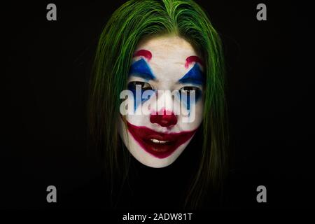 Ragazza con un trucco da clown ride follemente su sfondo scuro. Foto Stock