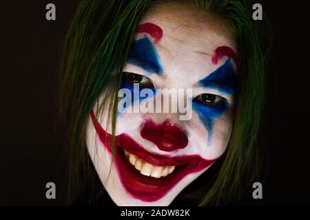 Ragazza con un trucco da clown ride follemente su sfondo scuro. Foto Stock