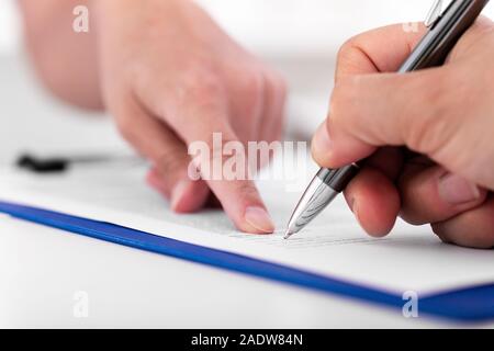 L uomo è la firma di un documento su un blu appunti, mani di una donna in background Foto Stock