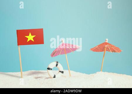 Bandiera in miniatura del Vietnam sulla spiaggia con ombrelloni colorati e salvagente. Concetto di viaggio, Tema estivo. Foto Stock