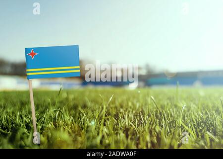 Stick miniaturizzato Aruba bandiera su erba verde, vicino campo di sole. Lo sfondo dello stadio, copia spazio per il testo. Foto Stock