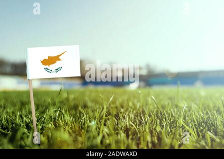 Stick miniaturizzato Bandiera di Cipro su erba verde, vicino campo di sole. Lo sfondo dello stadio, copia spazio per il testo. Foto Stock