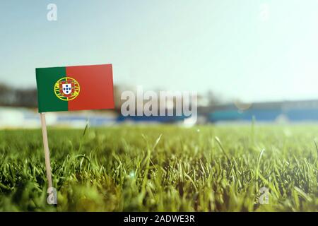 Stick miniaturizzato Portugal flag su erba verde, vicino campo di sole. Lo sfondo dello stadio, copia spazio per il testo. Foto Stock