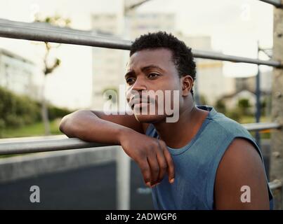 Close-up verticale di pensosa americano africano giovane uomo appoggiato su di un bar presso la palestra park Foto Stock