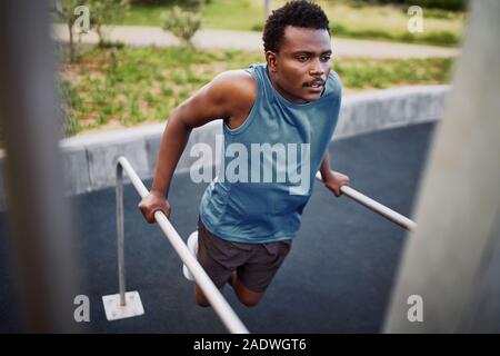 Giovane americano africano montare l'uomo facendo tricipiti dips su barre parallele in una palestra a cielo aperto park Foto Stock