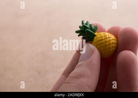 Mano che tiene un piccolo ananas miniatura su uno sfondo sul display Foto Stock