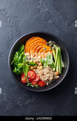 Sana insalata vegetariana. Arrosto di zucca, quinoa, pomodori, insalata verde. Ciotola di Buddha. Sfondo di ardesia. Vista dall'alto. Foto Stock