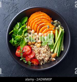 Sana insalata vegetariana. Arrosto di zucca, quinoa, pomodori, insalata verde. Ciotola di Buddha. Sfondo di ardesia. Vista dall'alto. Foto Stock