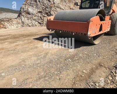 Rullo vibrante comprime il terreno di una superficie stradale durante la guida su strada con opere di costruzione. Movimento terra, scavi, scavando sui terreni rocciosi. Foto Stock