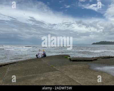 Un giovane seduto su una battuta di cemento che si affaccia sul Mare dei Caraibi in Puerto Limon Costa Rica. Foto Stock