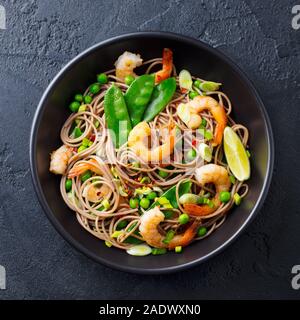 Friggere le tagliatelle con verdure e gamberi in nero ciotola. Sfondo di ardesia. Vista superiore Foto Stock