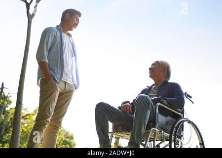 Giovani asiatici adulto uomo parlando con sedia a rotelle legato padre Felice e sorridente Foto Stock