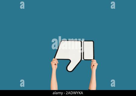 Mani tenendo il segno di antipatia su blu di sfondo per studio. Lo spazio negativo per inserire il tuo testo o immagine, pubblicità. Social media, che mostra il significato, comunicazione, gadget, moderne tecnologie. Foto Stock