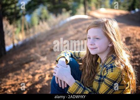 Giovane e bella rossa ragazza seduta al sole sul sentiero di montagna Foto Stock