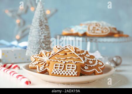 Piastra con biscotti di Natale, di alberi di Natale, giocattoli, scatole regalo sul tavolo bianco, contro sfondo blu, primo piano Foto Stock