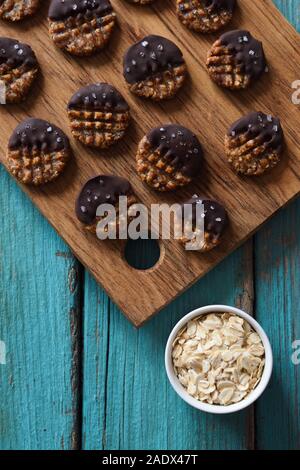 Materie vegane senza glutine e senza zucchero biscotti al cioccolato e sale servita con fiocchi d'avena su sfondo blu top view copyspace Foto Stock