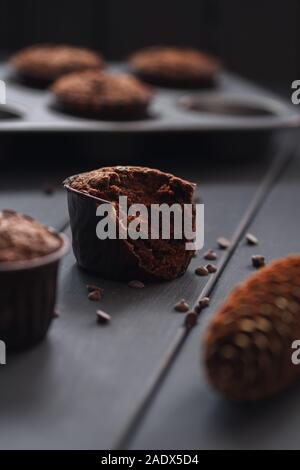 Hygge accogliente dessert. Mezza mangiata gustosi muffin al cioccolato con piccole scaglie di cioccolato su sfondo scuro in verticale Foto Stock