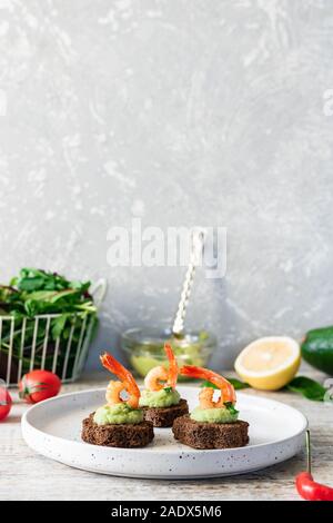 Crostini con musulmani di avocado e gamberi aglio sul pane marrone. Semplice e facile snack per feste e banchetti. Cibo confortevole. Foto Stock