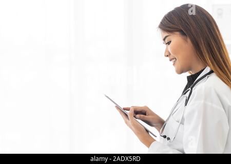 Ritratto femminile fiducioso medico professionista medico permanente e utilizzare digitale compressa nella camera di esame in ospedale. Faccia positiva espressione Foto Stock