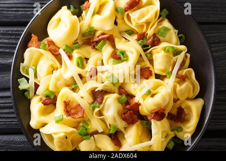 La pasta italiana tortelloni con pancetta e formaggio e cipolle verdi close-up in una piastra sul tavolo. parte superiore orizzontale vista da sopra Foto Stock