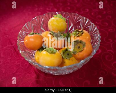 Persimmons mature aka sharon frutto kaki aka sul vetro di un cesto di frutta Foto Stock