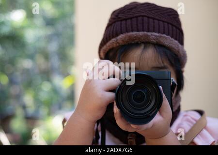 Ritratto di carino bambina in lana hat di scattare una foto con la fotocamera digitale su sfondo sfocato. Concetto di fotografia Foto Stock