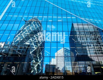 Il Gherkin è visto in una riflessione int egli lato del bisturi nel quartiere finanziario della City di Londra, Regno Unito Foto Stock