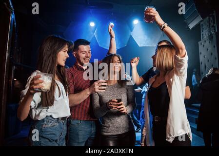 Non essere timido, mostra le tue mosse. Felice la gente ballare nel lussuoso night club insieme con bevande differenti nelle loro mani Foto Stock