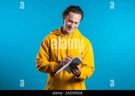 Giovane uomo bello controlla i documenti, bollette, relazione. Imprenditore isolato su sfondo blu. È soddisfatto con il lavoro del personale aziendale Foto Stock