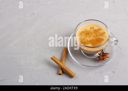 Masala tè in un bicchiere di vetro con anice e cannella e zenzero su sfondo grigio Foto Stock