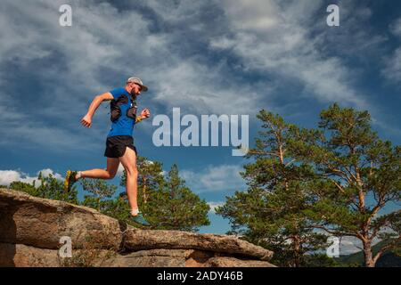 Runner maschio in esecuzione su di un sentiero di montagna. Atleta corre lungo il bordo della roccia. Uomo in maglia blu e pantaloncini neri all'aperto di formazione Foto Stock