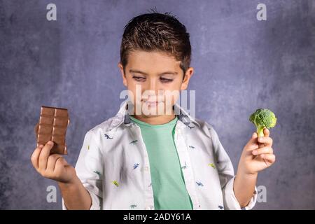 Ragazzino scegliendo tra i broccoli e cioccolata Foto Stock