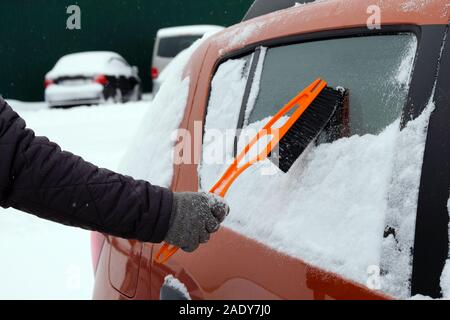 Spazzola in mano mans. Uomo in grigio guanti cancella arancione auto da neve. Rimuovere il sacco di neve da auto. Foto Stock