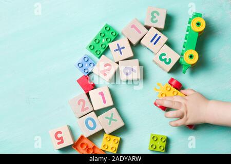 Bambini che giocano con i cubi di legno con numeri e colorati mattoni giocattolo su un turchese sullo sfondo di legno. Il Toddler numeri di apprendimento. La mano di un bambino takin Foto Stock