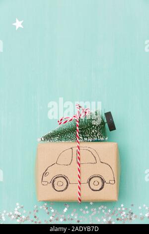 Vista dall'alto sul regalo di Natale avvolto in artigianato carta regalo decorata con disegno auto con albero di Natale sul turchese sullo sfondo di legno con spumante s Foto Stock