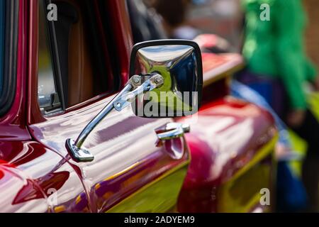 Antiquariato classico americano rosso raccoglitore lato auto specchietto cromato vista ravvicinata, persone in background durante outdoor vecchie auto show Foto Stock