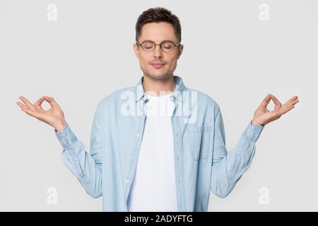 Rilassate la millenaria man standing meditando in studio con gli occhi chiusi Foto Stock