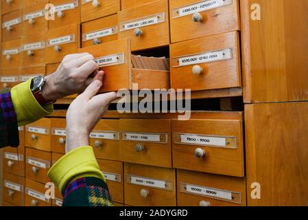 La mano di una persona apre una Library card file o directory. Concetto di database. Armadio antico in biblioteca con scatole per la memorizzazione di informazioni. Foto Stock