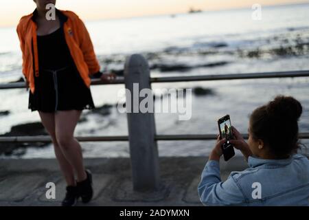 Gli amici di scattare foto con telefoni cellulari lungo il Greenpoint promenade nel Sud Africana di porto della città di Cape Town Foto Stock