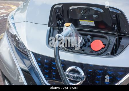 La Nissan Leaf auto elettrica essendo ricaricata presso il punto di ricarica a Warwick alla stazione di servizio sulla M 40 in autostrada in Inghilterra, Regno Unito Foto Stock