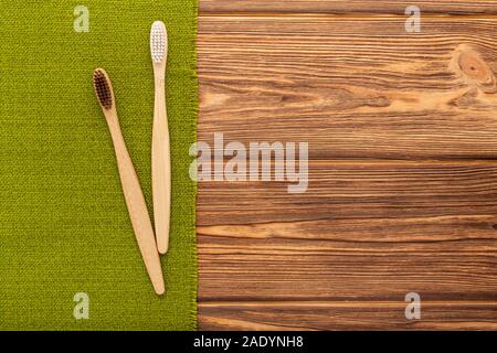 Gli spazzolini da denti di bambù sul verde su sfondo di legno. Lay piatto con copia spazio. Bagno naturale prodotti. Naturali biodegradabili spazzolino da denti di bambù. Eco Foto Stock