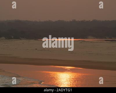 Fumo foschia al tramonto sulla spiaggia, riflesso sulle scintillanti acque di mare color arancio, sulla costa australiana Foto Stock