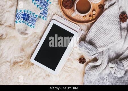 Tablet con schermo vuoto, un maglione pesante e calzini e una tazza di caffè sulla pelliccia Foto Stock