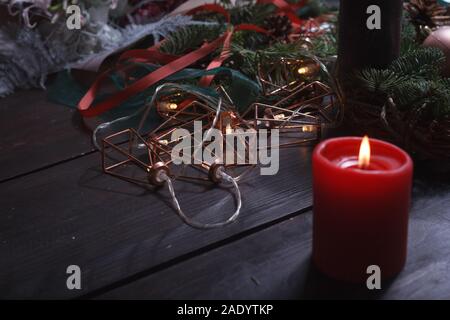 Close-up di un accogliente desktop di un fioraio con candele accese durante la creazione di una ghirlanda di Natale, il fuoco selettivo Foto Stock