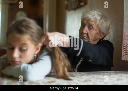 Donna anziana trecce suo nipote di capelli. Foto Stock