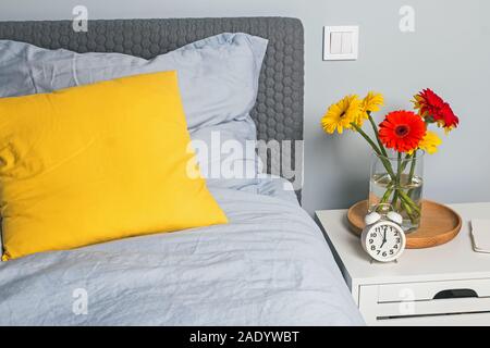 Camera moderna con interni luminosi cuscini decorativi sul letto e brigh fiori. Foto Stock