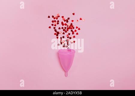 Coppa mestruale con rosso a forma di cuore di paillettes che simboleggiano le mestruazioni. Foto Stock