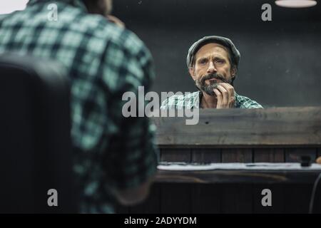 Uomo di mezza età accigliata mentre si tocca la sua barba Foto Stock