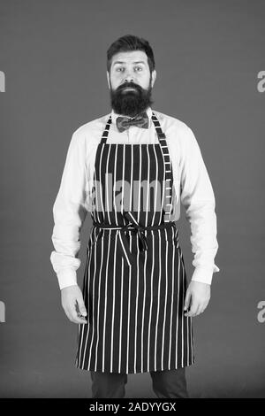 Io sono totalmente a vostro servizio. Un uomo servo. Uomo Barbuto che indossa la bib grembiule. L'uomo cook con barba e baffi in cucina il grembiule. Elegante uomo cameriere o barista. Foto Stock