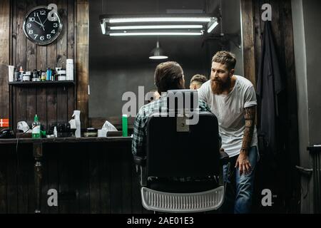 Attento barbiere appoggiata al client e a parlare con lui Foto Stock
